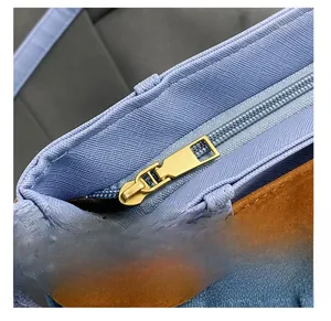 Detail view showing blue canvas fabric, brown trim, and premium gold metal zipper