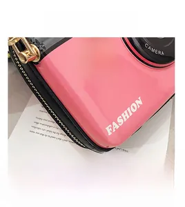 Detailed close-up of pink camera-shaped crossbody bag with gold chain and fashion text