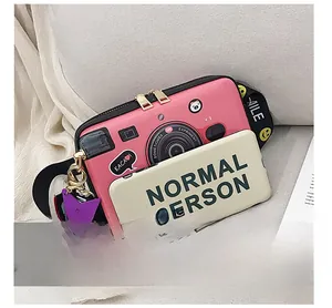 Detailed view of a pink camera-shaped crossbody bag with a smile star charm and phone size comparison
