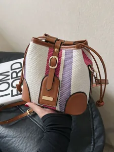 Striped canvas bucket bag with leather trim and gold hardware in a handheld pose