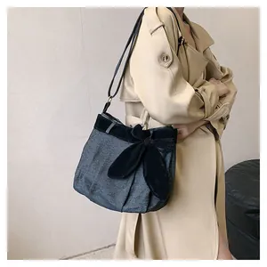 Detail of grey denim crossbody bag with large black velvet bow worn with khaki trench coat