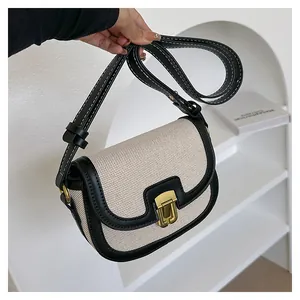 Detail of retro saddle bag with cream woven texture, black leather trim and gold buckle