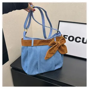 Detail of blue denim shoulder bag featuring a large brown suede bow and adjustable strap