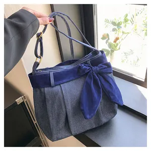 Detail of blue denim shoulder bag featuring a large decorative bow and velvet trim