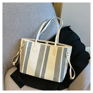 Detail van gestreepte canvas shopper met leren handvaten op een grijze stoel