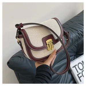 Detail of saddle bag with beige woven texture, burgundy leather, and gold buckle