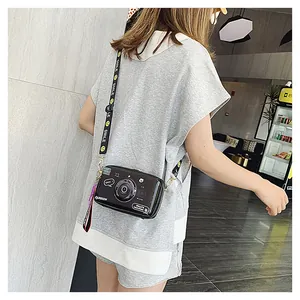Detail of camera-shaped crossbody bag featuring fashion text and a smiley face nylon strap