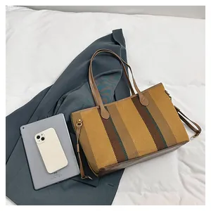 Detail van gestreepte canvas shopper met bruine leren hengsels en geweven textuur