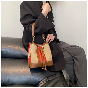 Detail of striped bucket bag featuring brown leather strap and gold-tone metal hardware