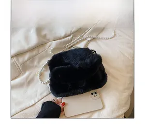 Detail view of black plush shoulder bag with pearl chain next to a smartphone for size