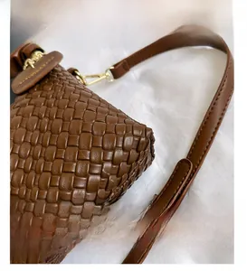 Détail de la texture en cuir tressé marron avec crochet métallique doré et bandoulière réglable