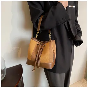 Detail of woven bucket bag with brown leather trim and drawstring on a female model