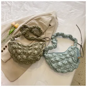 Detalle de bolsos de nube plisados en verde oliva y azul claro sobre una tela elegante
