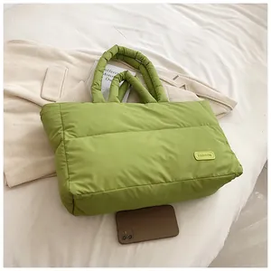 Détail d'un sac cabas matelassé vert avocat avec étiquette mode sur literie blanche