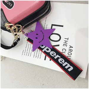 Detail of a purple wooden star charm and embroidered strap on a pink camera bag