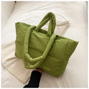 Détail d'un sac cabas matelassé vert olive avec étiquette de mode sur un lit blanc