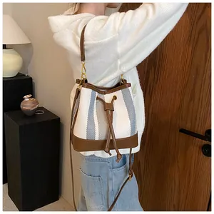 Detail of striped canvas bucket bag with brown leather trim and drawstring closure