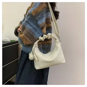 Detail of a creamy white crescent bag featuring ruched handle and leather texture