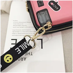 Close-up of pink camera bag with 'SMILE' wide strap and gold metal hardware hooks