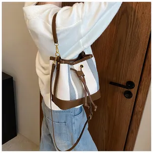 Detail of blue striped canvas bucket bag with brown leather trim and drawstring closure