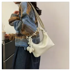 Detail of cream-colored shoulder bag featuring a ruched strap and woven ball tassel charm