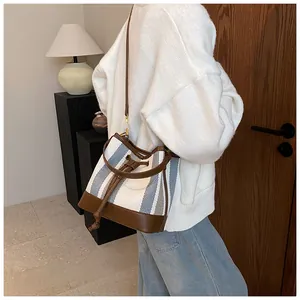 Detail of striped canvas bucket bag with brown leather trim and golden drawstring hardware