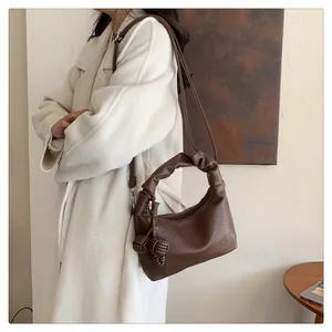 Close-up of a dark brown pleated crescent bag featuring an elegant braided knot charm