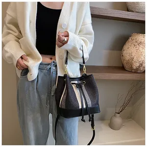 Fashionable striped bucket bag with drawstring closure and leather base shown on model