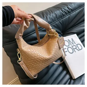 Détail d'un sac tressé abricot avec poignée plissée et chaîne dorée sur canapé cuir