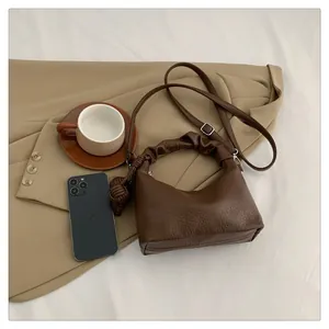 Detail of dark brown leather handbag with ruched handle and woven ball charm accessory