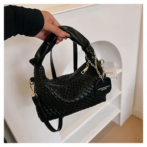 Détail d'un sac à main tressé noir avec chaîne dorée et poignée ronde épaisse