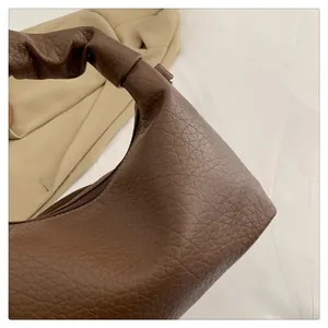 Close-up of brown pebbled leather texture and elegant ruched handle design on underarm bag
