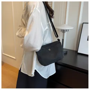 Detail of minimalist black canvas crossbody bag with metal button and zip closure