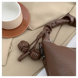 Close-up of pleated handle with woven leather knots and litchi texture on a brown tote