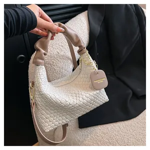 Détail d'un sac tressé blanc avec poignée froncée marron et chaîne dorée décorative