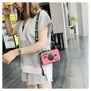 Pink camera-shaped hardshell crossbody bag with a wide smile patterned shoulder strap
