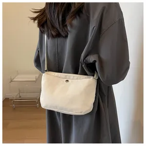 Detailed back view of an off-white canvas crossbody bag with adjustable strap on a model