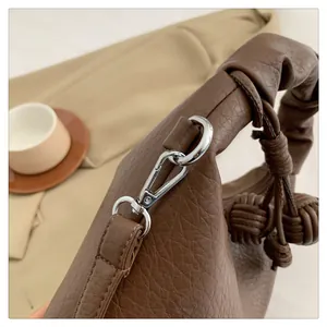 Detail of dark brown lychee grain leather bag featuring silver hooks and woven pendant
