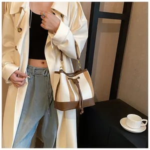 On-body shot of a striped canvas bucket bag with brown leather trim and gold hardware