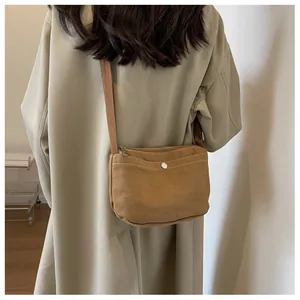 Detail of caramel canvas crossbody bag with front snap pocket worn over a trench coat