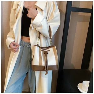 Detail of striped canvas bucket bag showing drawstring closure and brown leather trim