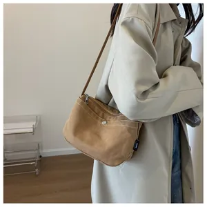 Detail of tan canvas crossbody bag with white stitching and metal button pocket