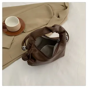 Detailed interior of dark brown leather tote featuring woven ball charm and soft lining