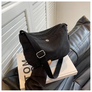 Detail of black canvas crossbody bag showing metal snap pocket and adjustable strap