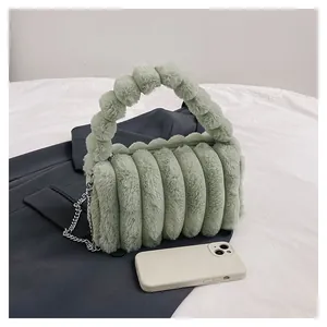 Detail of mint green plush handbag with vertical quilting and furry ball handle design