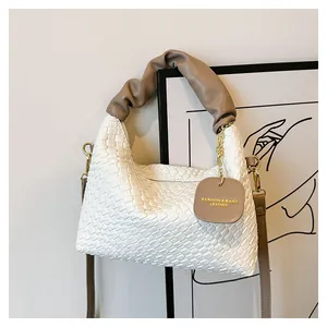 Gros plan d'un sac à main tressé blanc avec poignée plissée marron et étiquette cuir