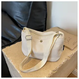 Minimalist beige canvas crossbody bag detail showing front pocket on a stone surface