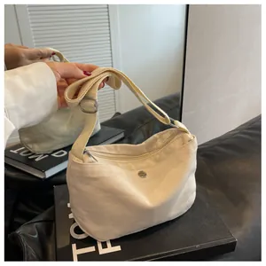Detail of off-white canvas crossbody bag featuring front pocket with silver metal snap button