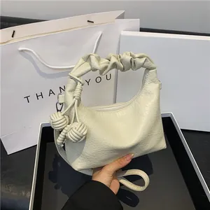 Minimalist beige leather hobo bag with pleated handle and ball charm detail