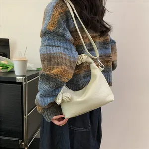 Minimalist creamy white crescent shoulder bag with knotted strap and textured leather finish
